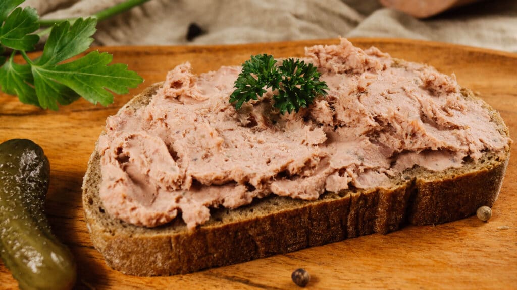 Brot mit Gutshofleberwurst bestrichen und Petersilie bestückt, angerichtet auf einem Holzbrett mit Gewürzgurke